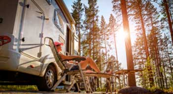 Woman sitting on chair outside RV in forest