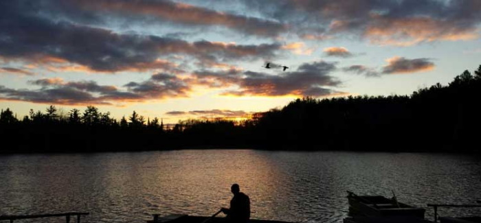 person sitting in boat looking over water sunset