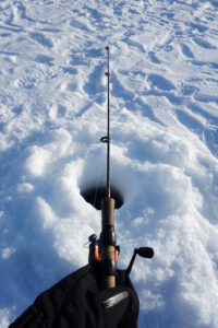 Waiting patiently at an ice fishing hole on a frozen lake. Shot from the first person perspective