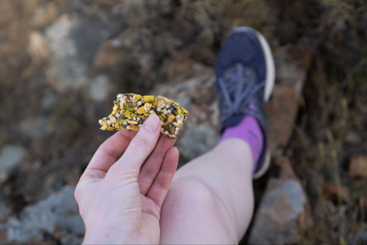 Close-up of a female hiker's hand as she holds a small piece of a protein bar.