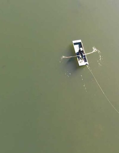 A minimalist overhead aerial photo of a small rowboat floating on the perfectly still, green-tinged water of a calm lake.