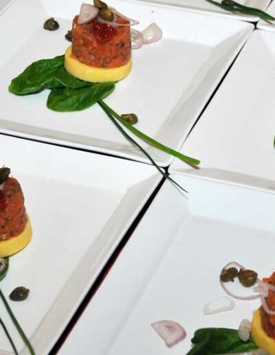 An elegant top-down view of multiple white appetizer plates, each beautifully arranged with gourmet hors d'oeuvres and colorful garnishes.