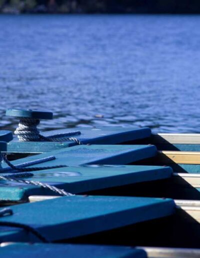 A row of bright blue and white canoes neatly stacked side-by-side along a wooden dock, set against deep blue water.