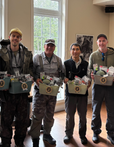 A row of five men standing inside the bright clubhouse banquet room, smiling while holding matching gift boxes or prizes.