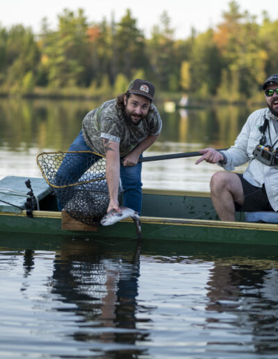Two anglers sitting in a green punt on the calm lake, preparing their fishing rods on a sunny day.