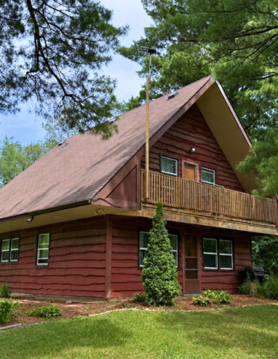 A beautiful two-story rustic log cabin guest cottage with a balcony surrounded by lush green forest trees.