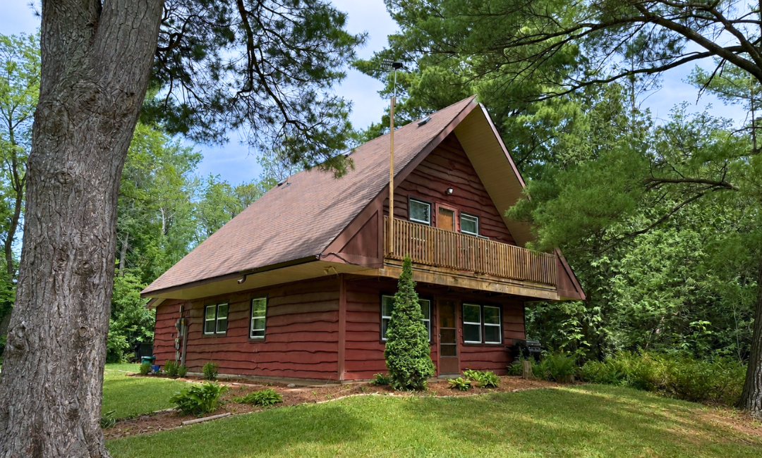 Franklin-Club-Log-Cabin-Cottage-Exterior A beautiful two-story rustic log cabin guest cottage with a balcony surrounded by lush green forest trees.