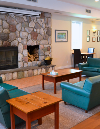 The spacious main clubhouse lounge featuring a large stone fireplace, cozy sofas, and dining seating.